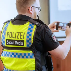 Ein Polizist mit einem Smartphone in der Hand (Symbolfoto)