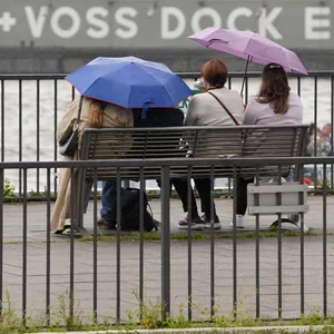 Passanten schützen sich mit Regenschirmen auf einer Sitzbank an den Landungsbrücken vor dem Regen