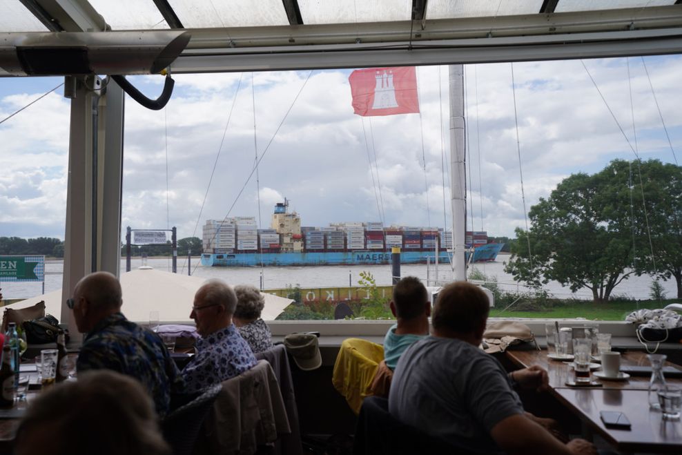 Ein Containerschiff fährt nach dem Verlassen des Hamburger Hafens auf der Elbe an der Schiffsbegrüßungsanlage „Willkomm Höft“ im Schulauer Fährhaus vorbei.