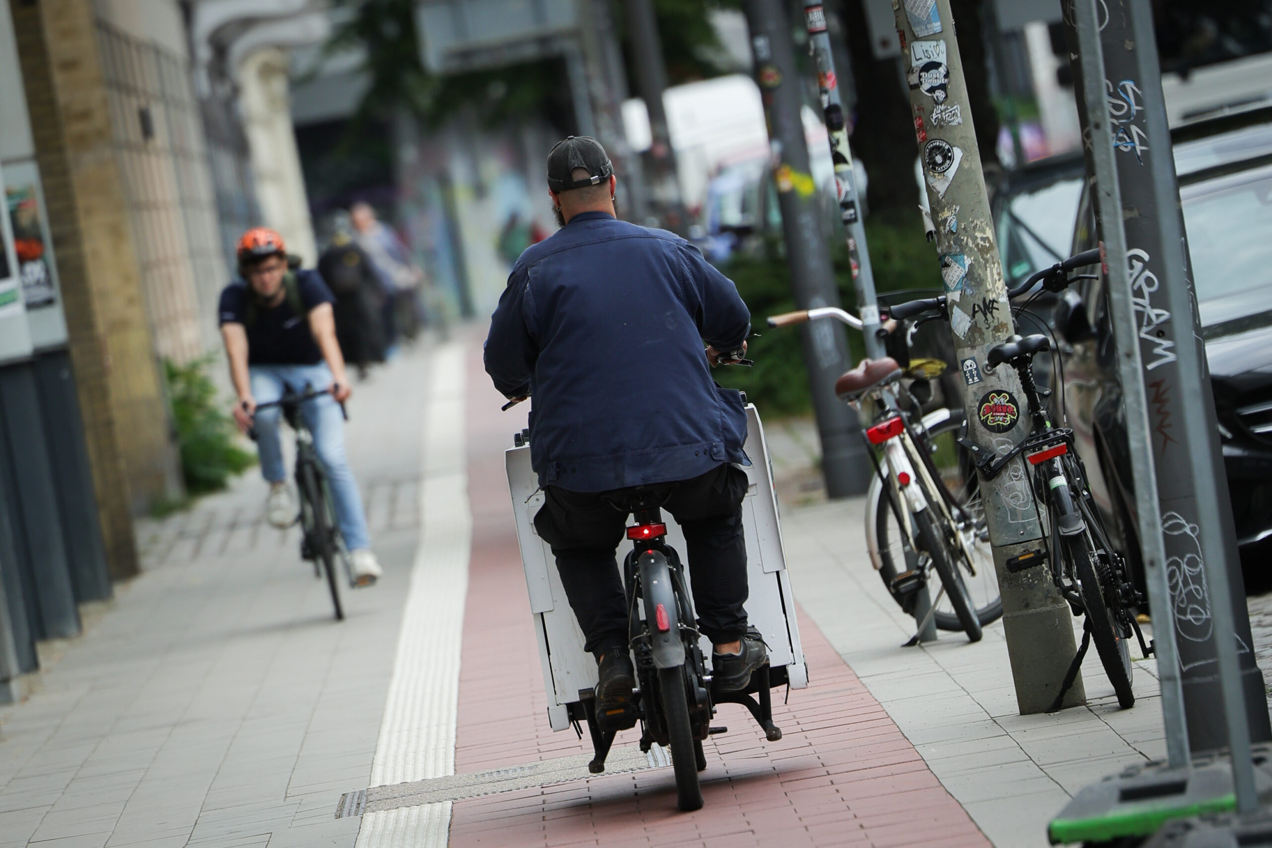 Ein Elektro-Lastenrad und ein Radfahrer begegnen sich auf einem Radweg in Hamburg-Altona. Angesichts von zunehmenden Einschränkungen für Autos in den Innenstädten setzen Logistikunternehmen auf Elektro-Lastenfahrräder.