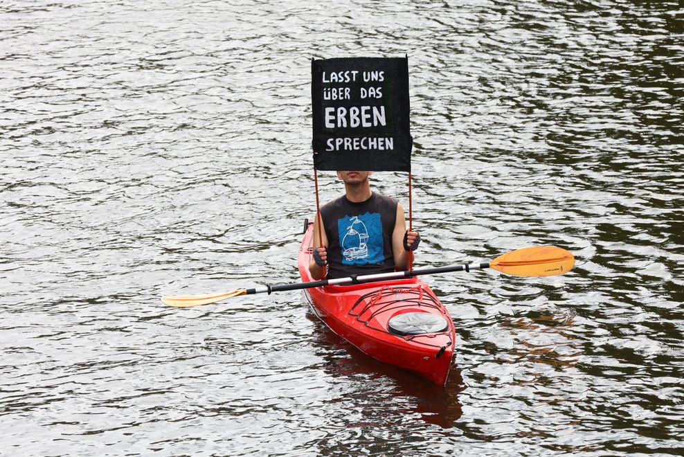 Ein Demonstrant in einem Kajak mit einem Plakat: „Lasst uns über das Erben sprechen.“