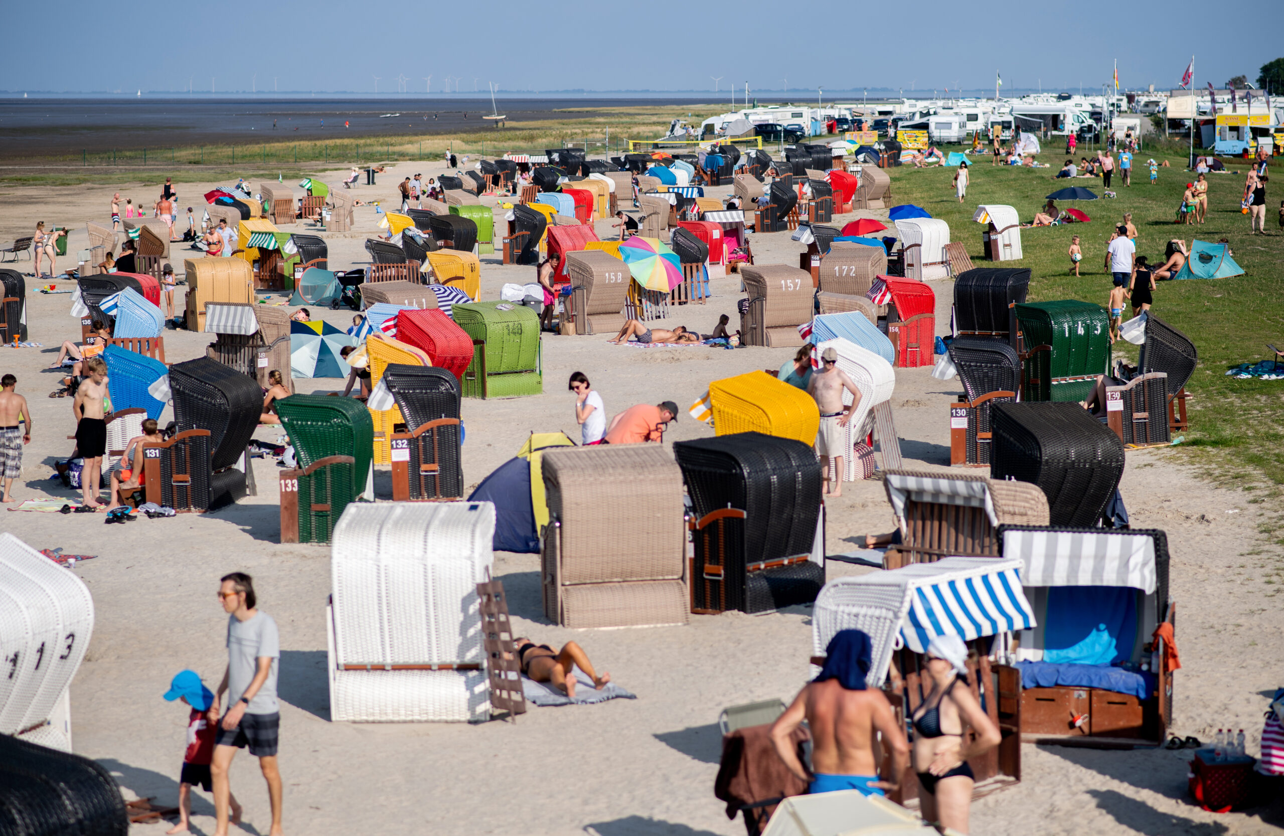 Zahlreiche Touristen sitzen bei sommerlichen Temperaturen in bunten Strandkörben am Strand von Dangast am Jadebusen.