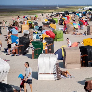 Zahlreiche Touristen sitzen bei sommerlichen Temperaturen in bunten Strandkörben am Strand von Dangast am Jadebusen.