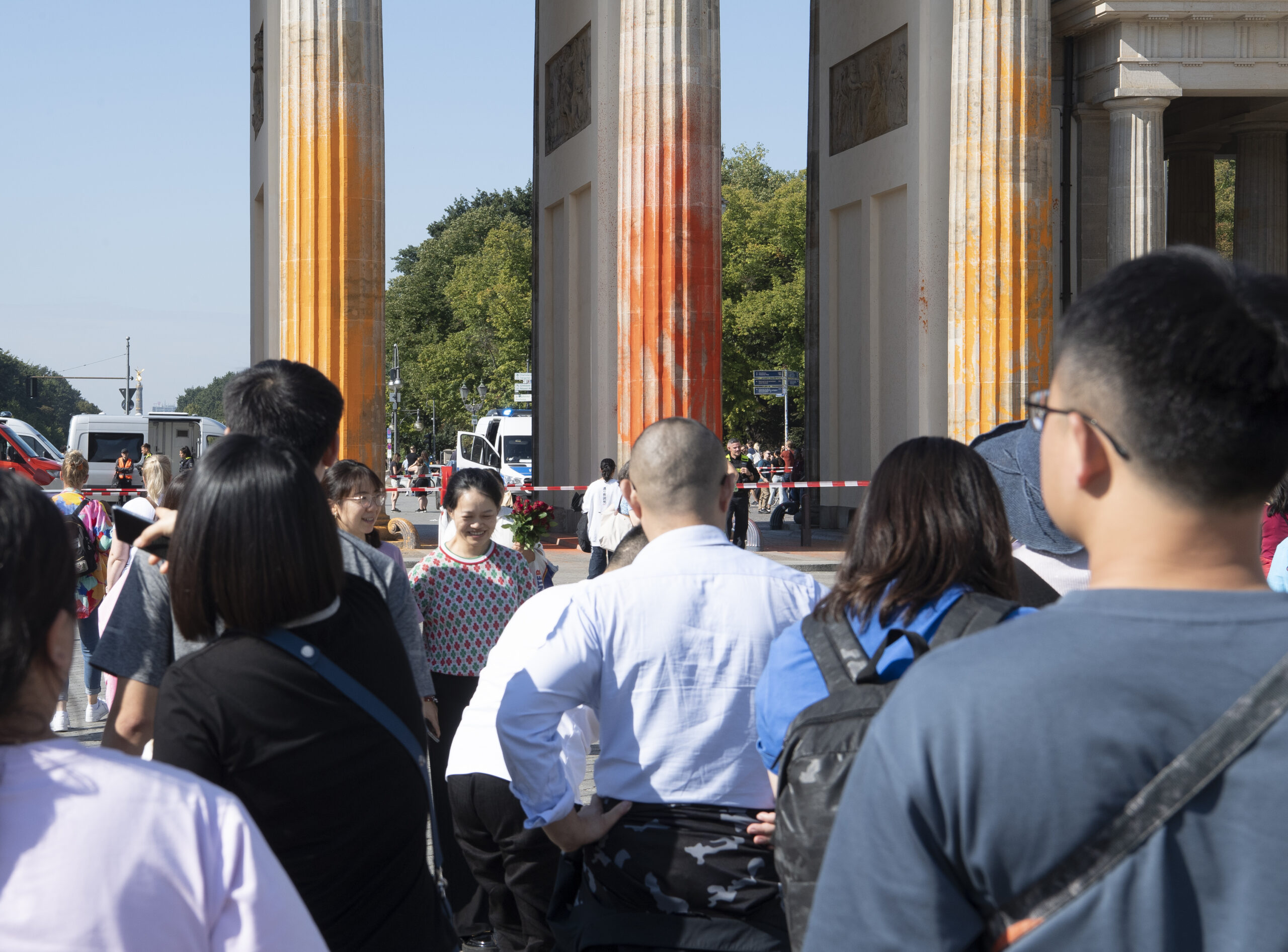 Touristen stehen vor dem Brandenburger Tor, das mit oranger Farbe angesprüht wurde.