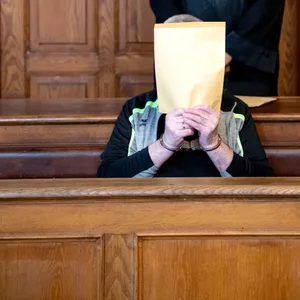 Der Angeklagte sitzt im Gerichtssaal und verbirgt sein Gesicht hinter einem Umschlag. Die Staatsanwaltschaft wirft dem 74-Jährigen vor, im März 2023 seine Ehefrau gewürgt und dann mit einer CO2-Kartusche auf den Hinterkopf geschlagen zu haben.