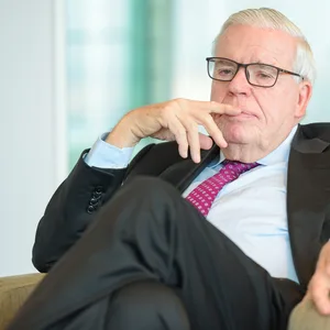 Klaus-Michael Kühne sitzt auf einem Sessel. Er trägt eine einen Anzug und sieht nachdenklich aus.