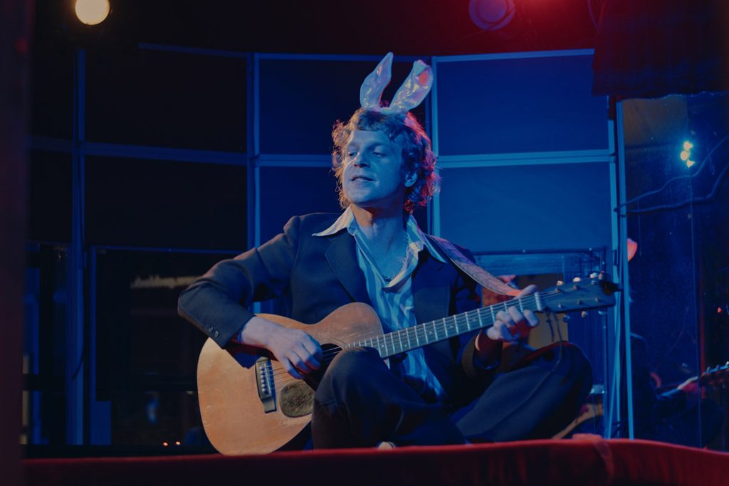 Musiker mit Gitarre und einem Haarraeif mit Hasenohren
