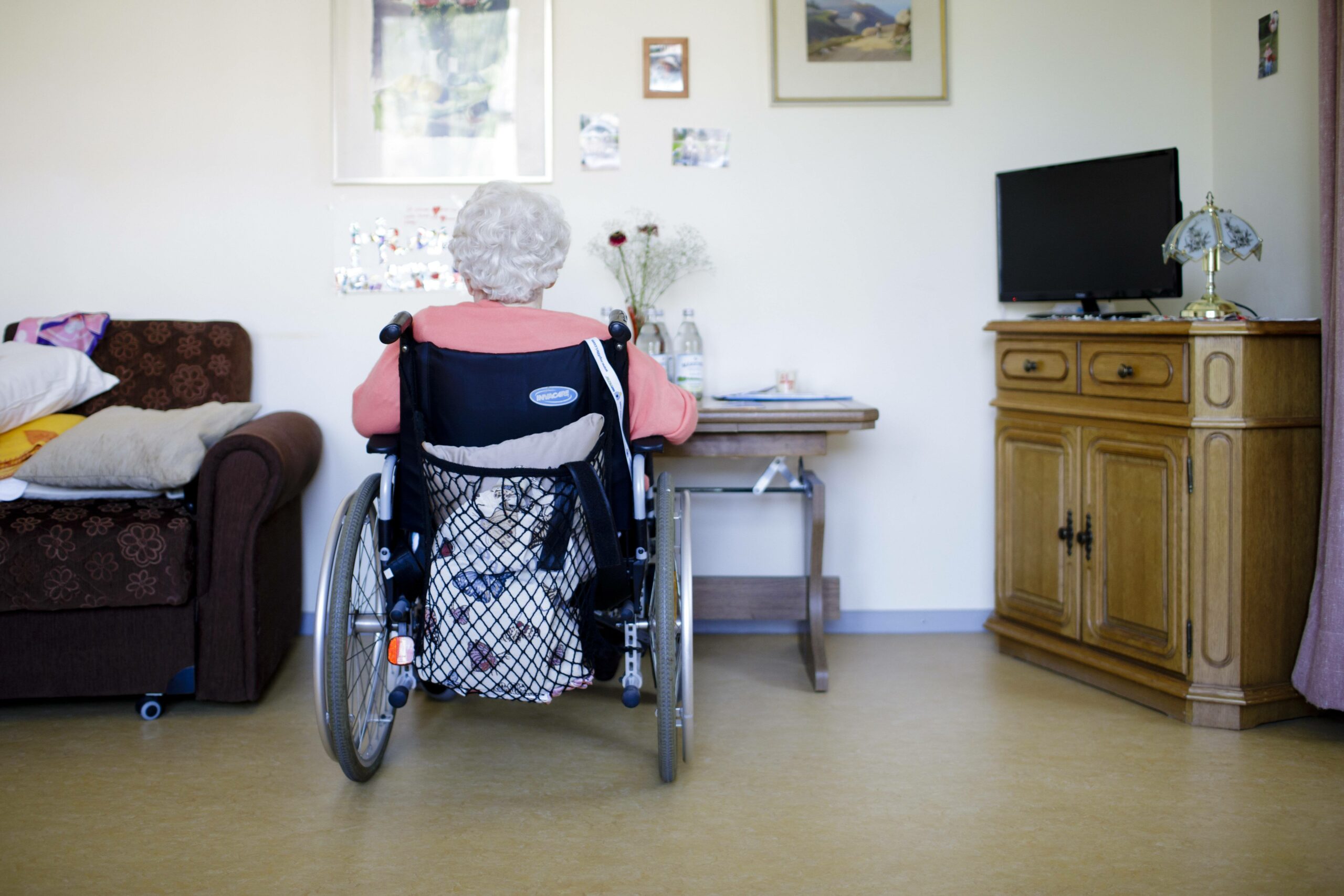 Eine ältere Frau im Rollstuhl sitzt in ihrem Zimmer vor einer Wand. (Symbolbild)