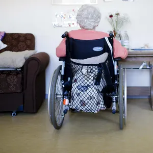 Eine ältere Frau im Rollstuhl sitzt in ihrem Zimmer vor einer Wand. (Symbolbild)