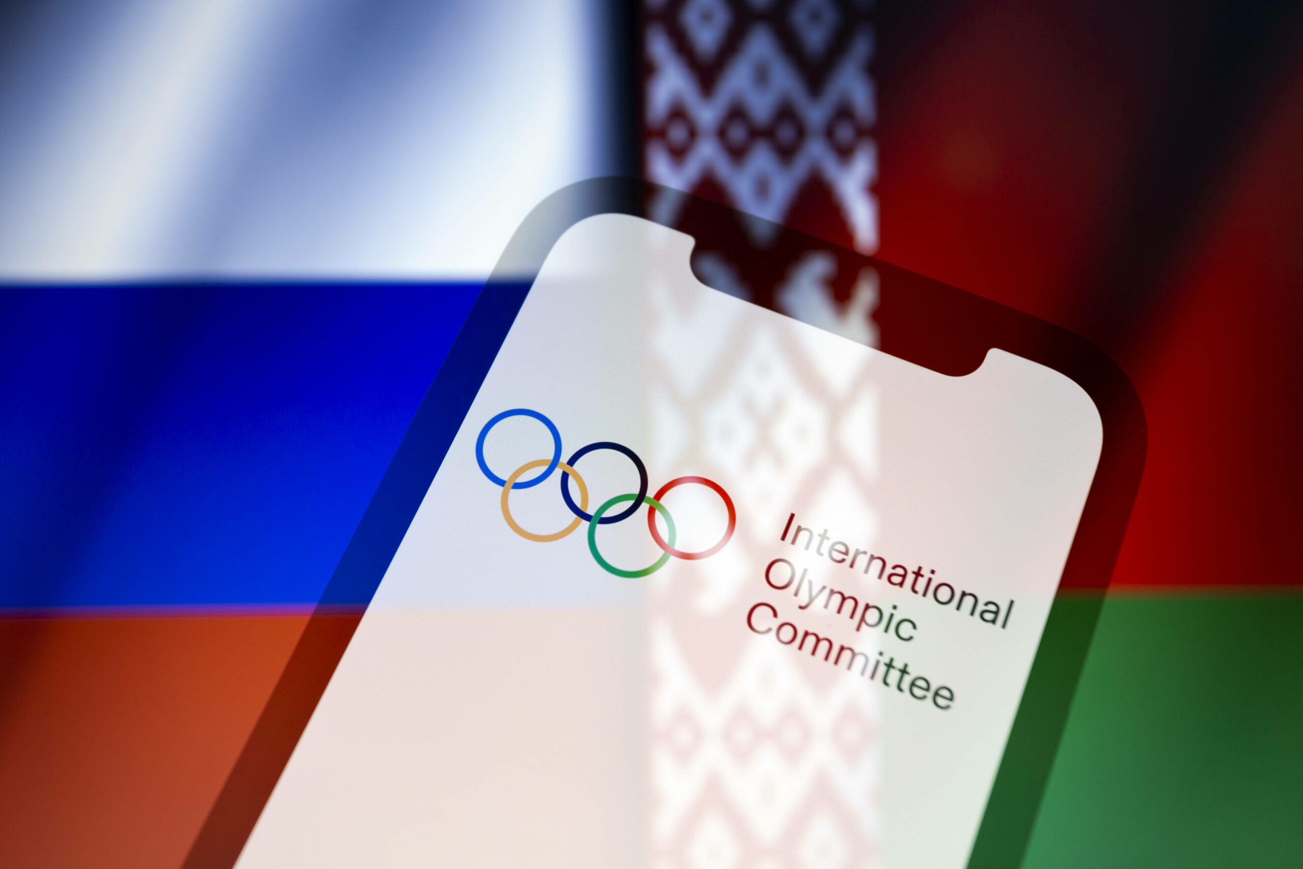Olympia-Logo vor den Flaggen von Russland und Belarus