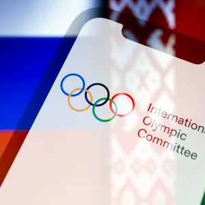 Olympia-Logo vor den Flaggen von Russland und Belarus