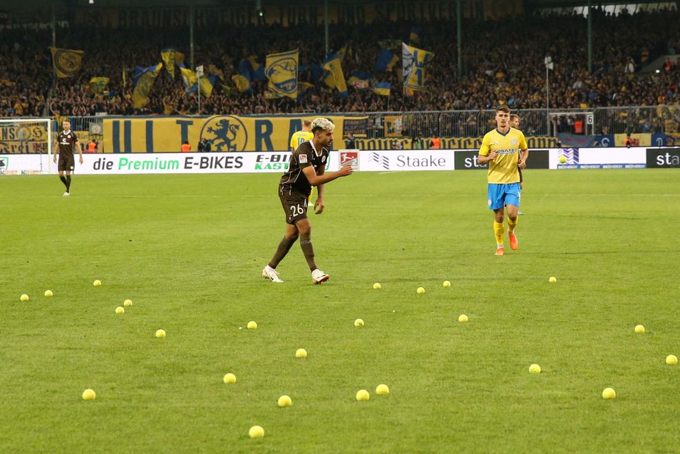 Elias Saad sammelt Tennisbälle auf, die St. Pauli-Fans in der Halbzeitpause auf den Braunschweiger Rasen geworfen haben.