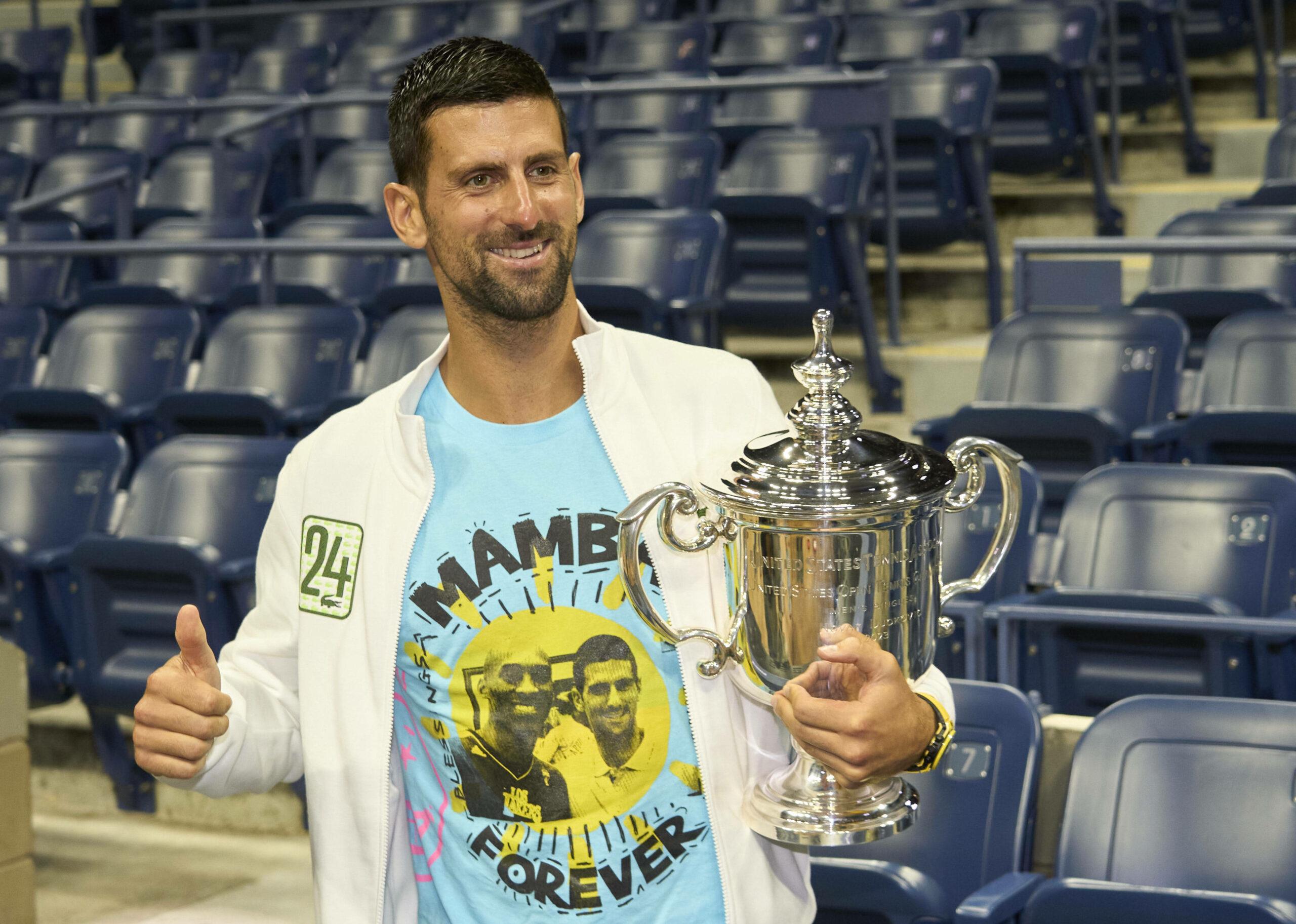 Novak Djokovic im T-Shirt mit einem Bild von ihm und Kobe Bryant präsentiert seine Trophäe.