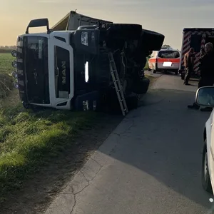 Ein Sattelzug liegt umgekippt auf einem Feld neben einer Straße.