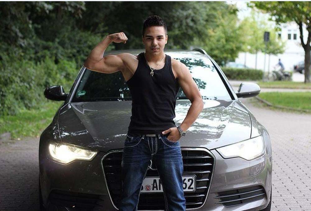 Tunahan Keser posiert vor einem Auto, er zeigt den Bizeps seines rechten Arms