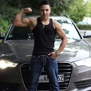 Tunahan Keser posiert vor einem Auto, er zeigt den Bizeps seines rechten Arms