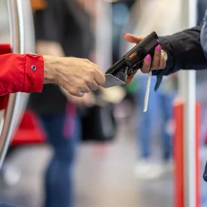 Eine Fahrkartenkontrolleurin (r.) kontrolliert mit einem elektronischen Lesegerät Fahrscheine. (Symbolbild)