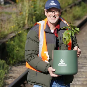 Peter Wohlleben, Förster und Bestsellerautor, hält einen Umtopf mit einem kleinen Kirschbaum im Bereich B auf Gleis 14 am Hamburger Hauptbahnhof.