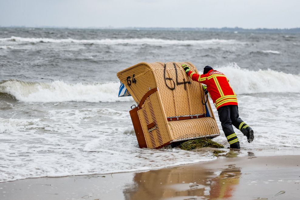 Ein Feuerwehrmann versucht, einen Strandkorb vor den Flutwellen der Ostsee zu sichern.