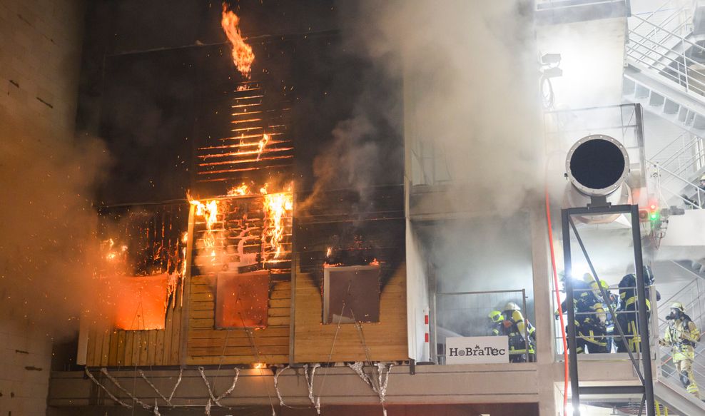 Feuerwehrkräfte löschen im Zentrum für Brandforschung (ZeBra) der Technischen Universität Braunschweig während eines Forschungsprojektes eine brennende Holzfassade.