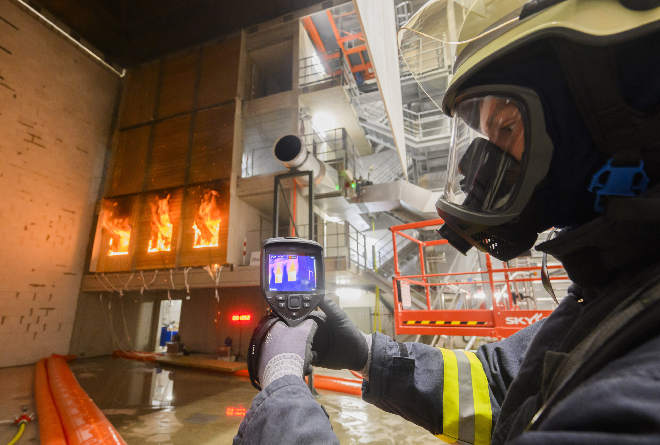 Ein Feuerwehrmann überprüft mit einer Wärmebildkamera im Zentrum für Brandforschung (ZeBra) der Technischen Universität Braunschweig während eines Forschungsprojektes eine brennende Holzfassade