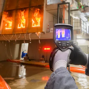 Ein Feuerwehrmann überprüft mit einer Wärmebildkamera im Zentrum für Brandforschung (ZeBra) der Technischen Universität Braunschweig während eines Forschungsprojektes eine brennende Holzfassade
