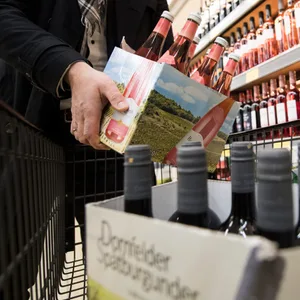 Jemand packt eine Kiste mit Wein in einen Einkaufswagen.