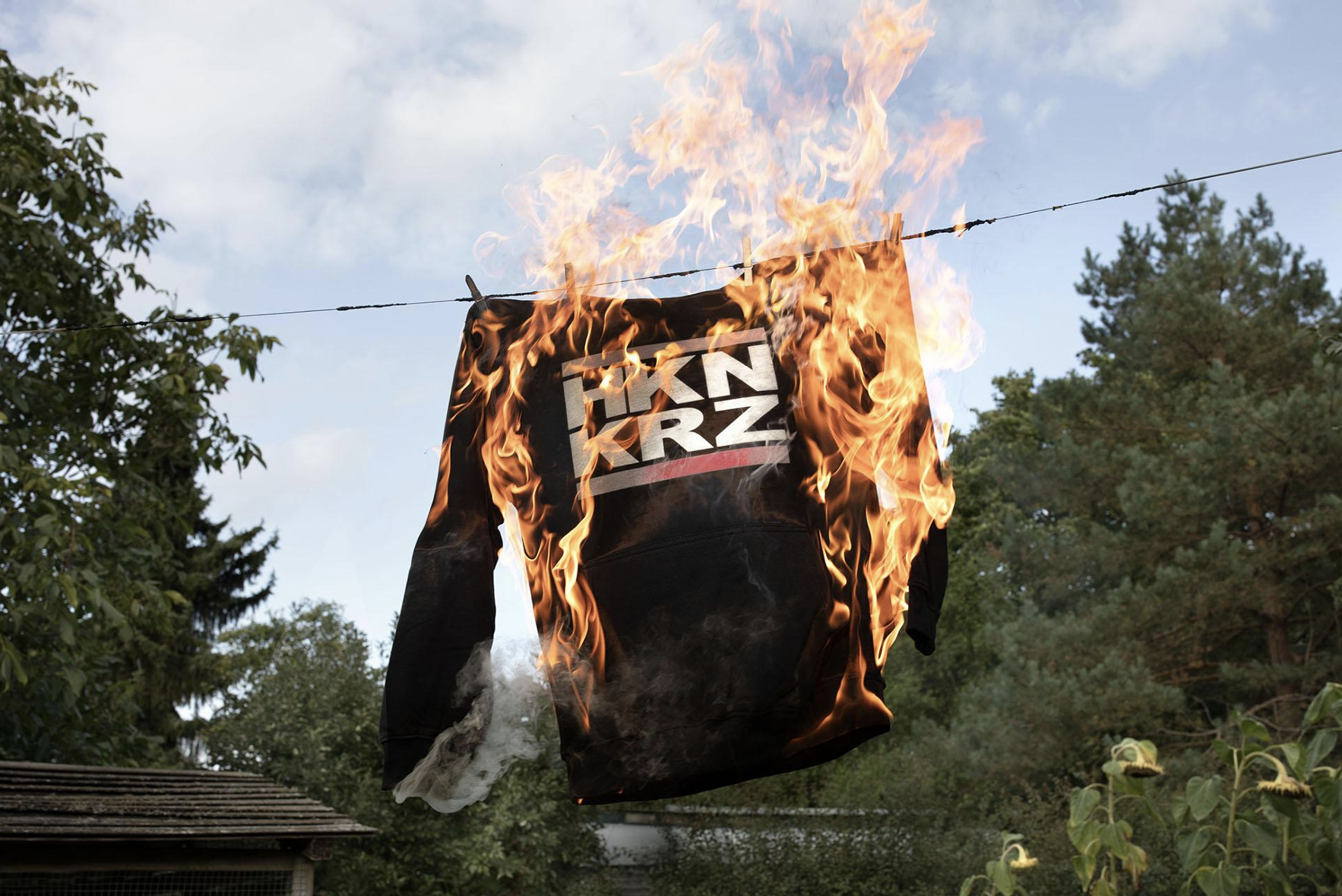 Ein Pullover mit der Aufschrift HKN KRZ (für Hakenkreuz) hängt brennend an einer Wäscheleine.