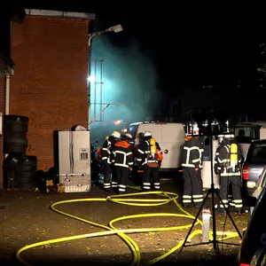 Feuerwehrleute stehen vor dem Gebäude, aus dem Rauch zieht.