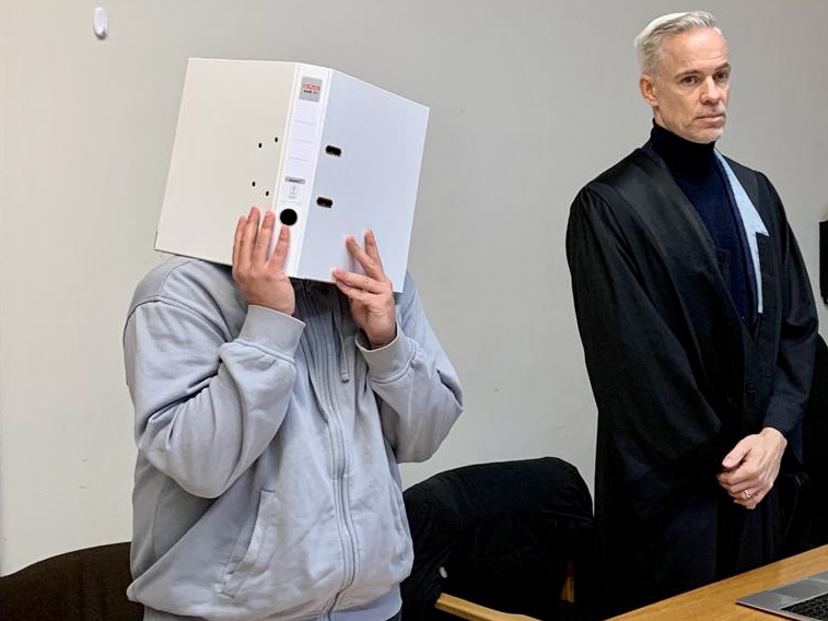 Der Angeklagte mit Aktenordner vor dem Gesicht, daneben sein Anwalt