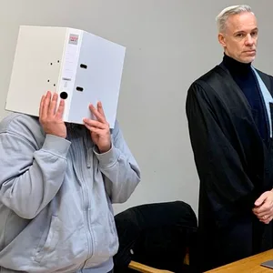 Der Angeklagte mit Aktenordner vor dem Gesicht, daneben sein Anwalt