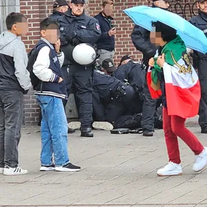 Eine Frau, die eine iranische Flagge trug, soll beleidigt worden sein. Im Hintergrund haben Polizisten ein Mann zu Boden gebracht.
