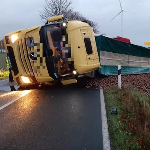 Ein Lkw liegt umgekippt auf der Straße, Tausende Kartoffeln sind auf dem Feld neben der Straße gelandet.