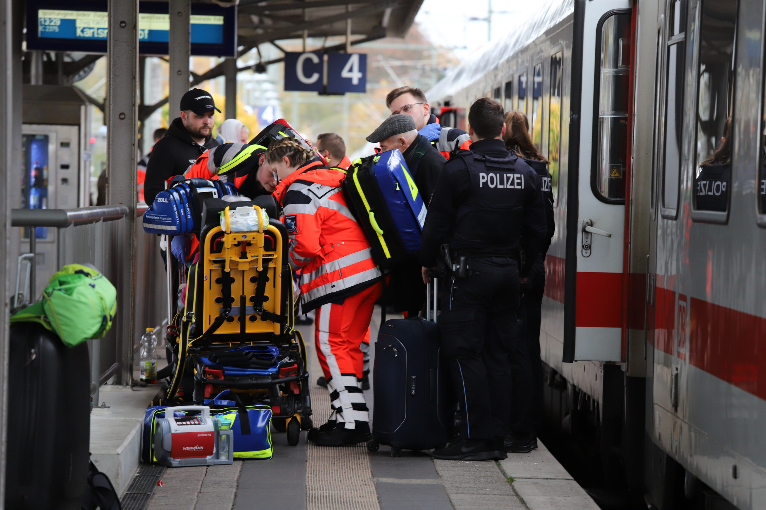 Rettungskräfte kümmern sich um eine verletzte Person. Polizeibeamte stehen neben dem in den Unfall verwickelten Zug.