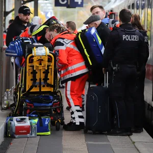 Rettungskräfte kümmern sich um eine verletzte Person. Polizeibeamte stehen neben dem in den Unfall verwickelten Zug.