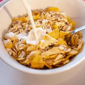 Milch fließt in eine Schale mit Cornflakes
