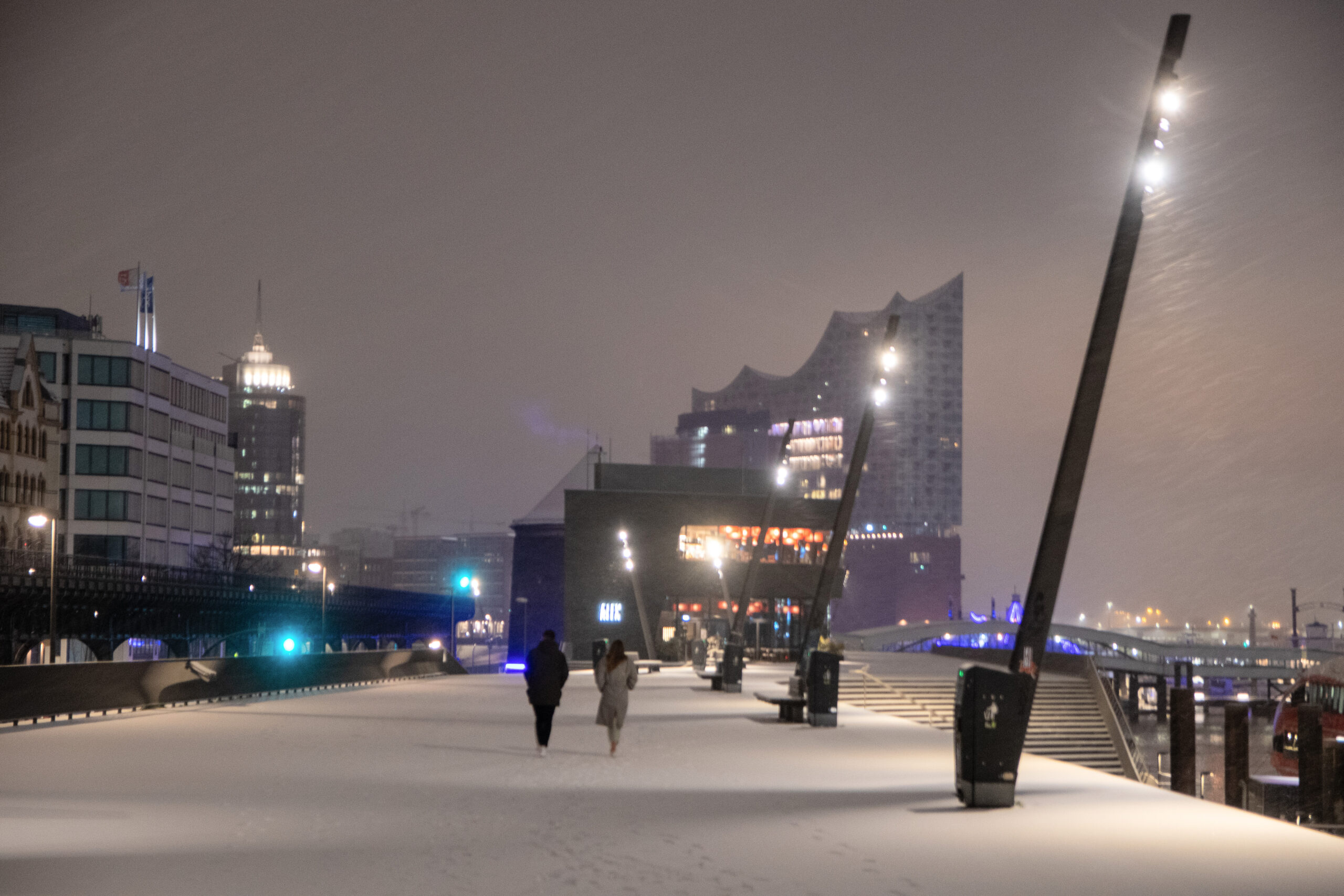 Passanten gegen über einen schneebedeckten Fußweg, im Hintergrund die Elbphilharmonie Hamburg.