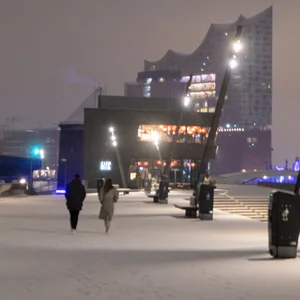 Passanten gegen über einen schneebedeckten Fußweg, im Hintergrund die Elbphilharmonie Hamburg.