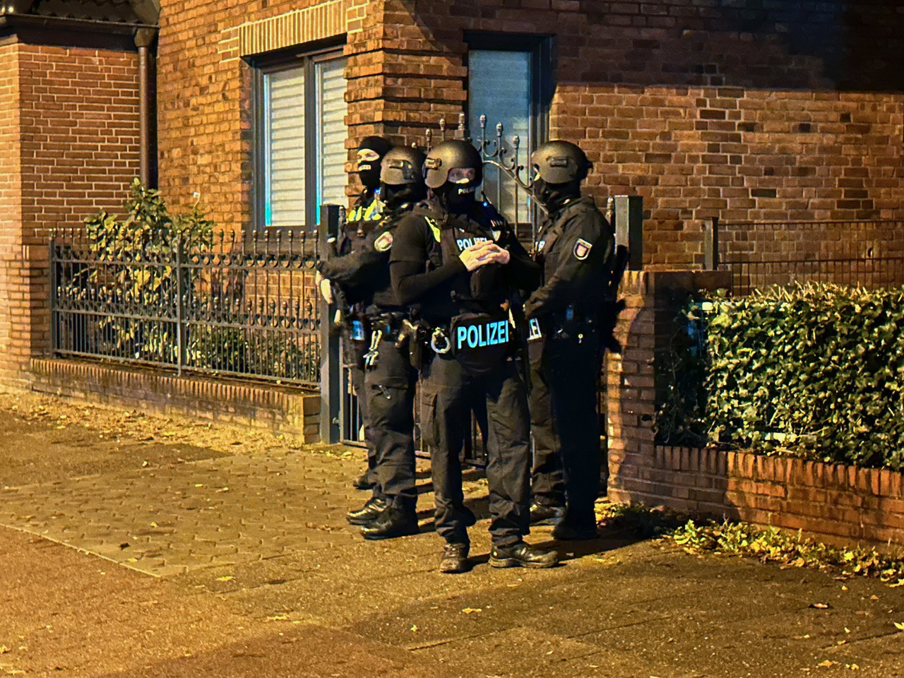 Polizisten stehen in schusssicherer Ausrüstung und mit Maschinenpistolen bewaffnet vor der Wohnanschrift des Verdächtigen an der Julius-Vosseler-Straße.