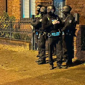 Polizisten stehen in schusssicherer Ausrüstung und mit Maschinenpistolen bewaffnet vor der Wohnanschrift des Verdächtigen an der Julius-Vosseler-Straße.