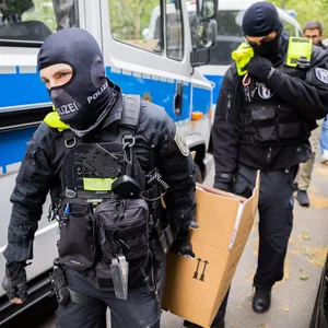 Polizisten tragen bei einer Hausdurchsuchung in Berlin-Kreuzberg einen Karton zu einem Fahrzeug.