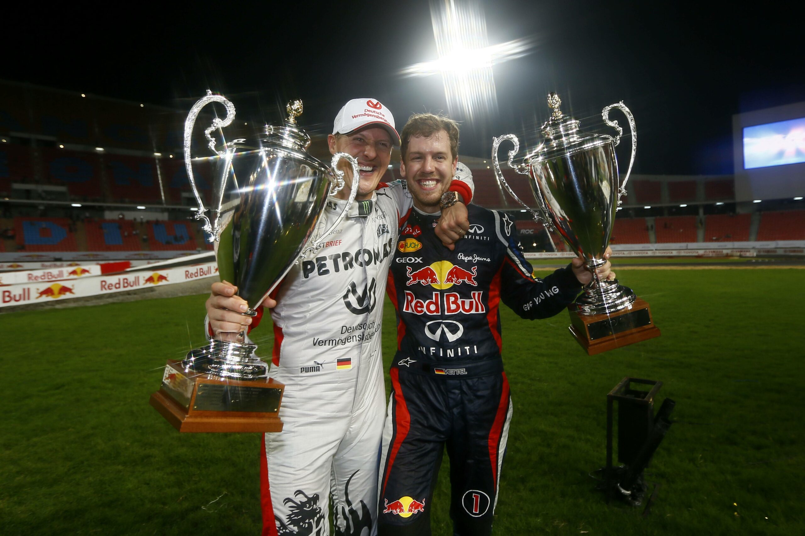 Michael Schumacher und Sebastian Vettel in Rennanzug und Pokal in der Hand