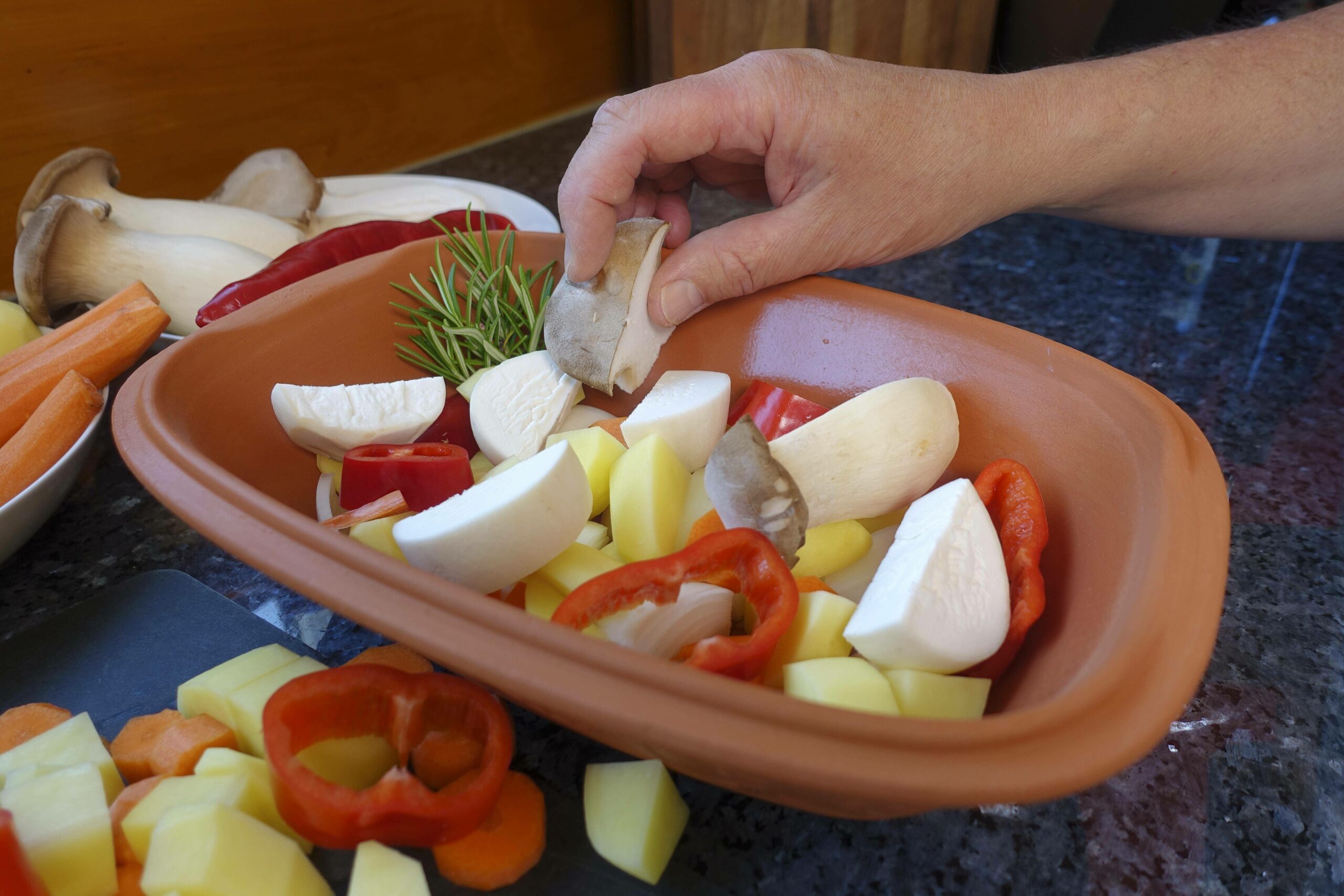 Eine Person bereitet verschiedene Gemüse in einem Römertopf zu. (Symbolbild)