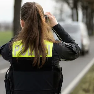 Ein Beamtin der Polizei steht mit einem Laser für die Geschwindigkeitsmessung von Fahrzeugen an einer Straße. (Symbolbild)