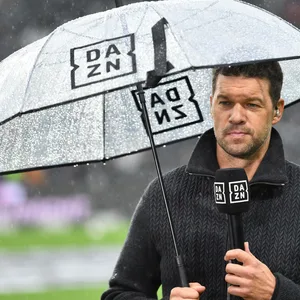 Michael Ballack mit DAZN-Mikrofon in der Hand steht unter einem DAZN-Regenschirm.