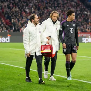 Bayern Münchens Jamal Musiala geht neben den Mannschaftsärzten vom Platz.