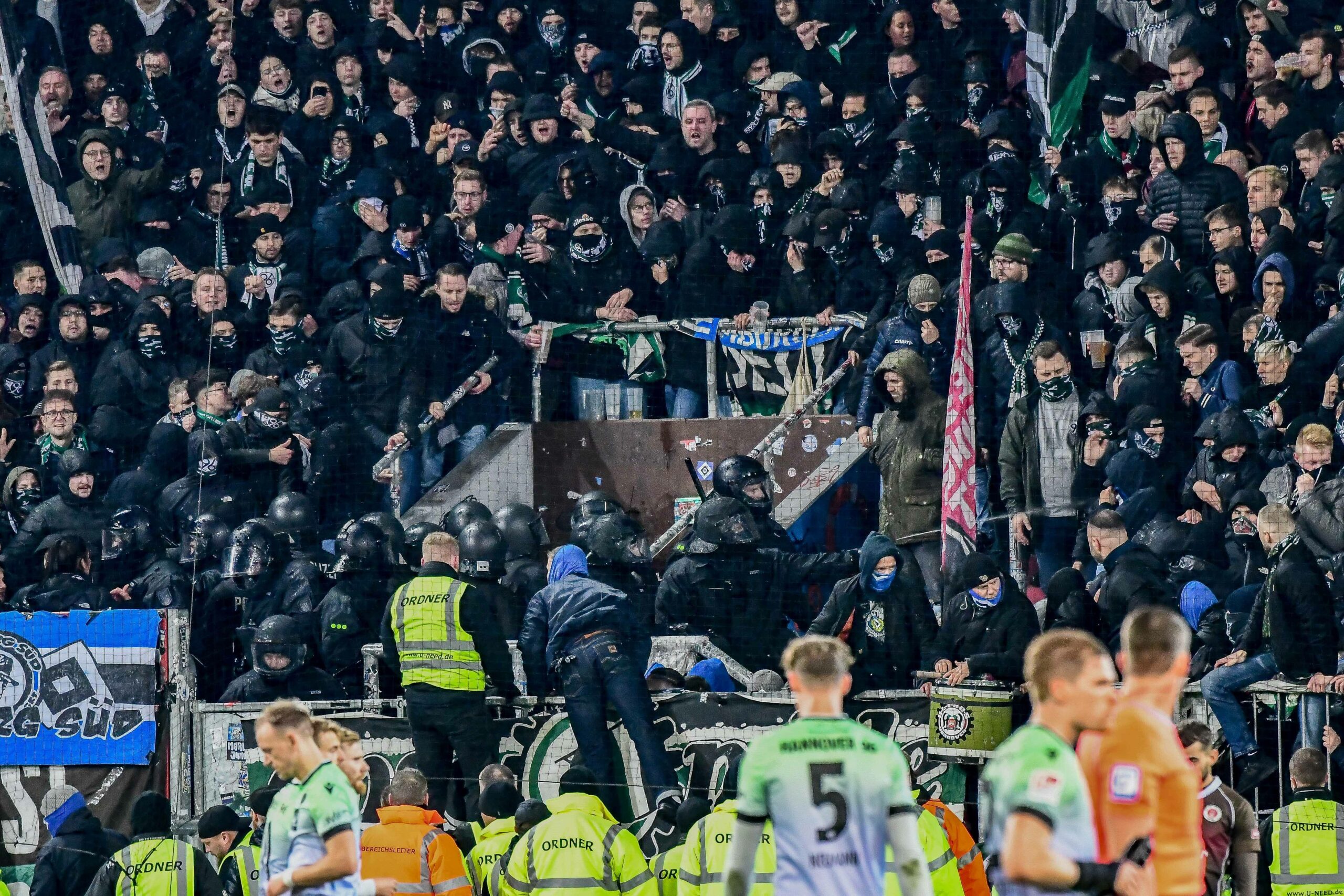 Polizei und Fans im Fanblock, davor eine Reihe von Ordnern