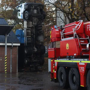 Im Vordergrund ein Wagen der Feuerwehr, hinten der Lkw, der senkrecht auf dem Heck steht