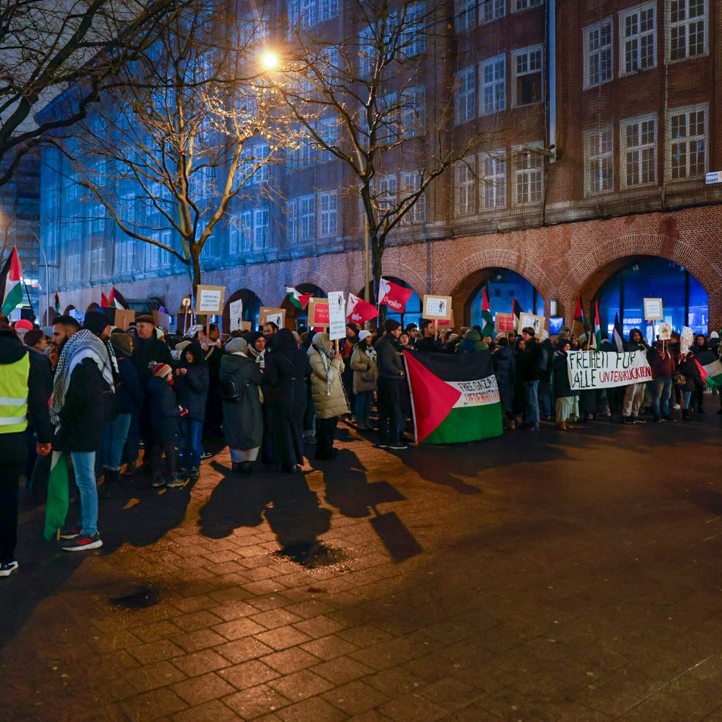 Mindestens 120 Menschen haben sich am Freitagabend zu einer pro-palästinensischen Demo in Hamburg versammelt. EInige halten Flaggen und Transparente hoch. Ordner und die Polizei begleiten die Demo.