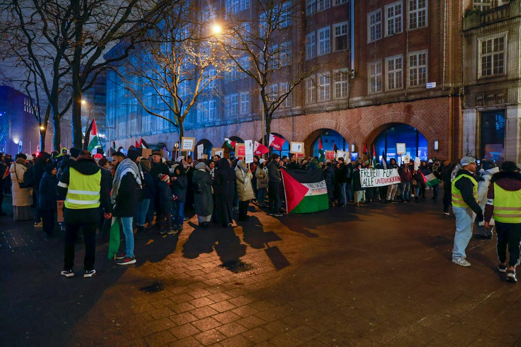 Mindestens 120 Menschen haben sich am Freitagabend zu einer pro-palästinensischen Demo in Hamburg versammelt. EInige halten Flaggen und Transparente hoch. Ordner und die Polizei begleiten die Demo.